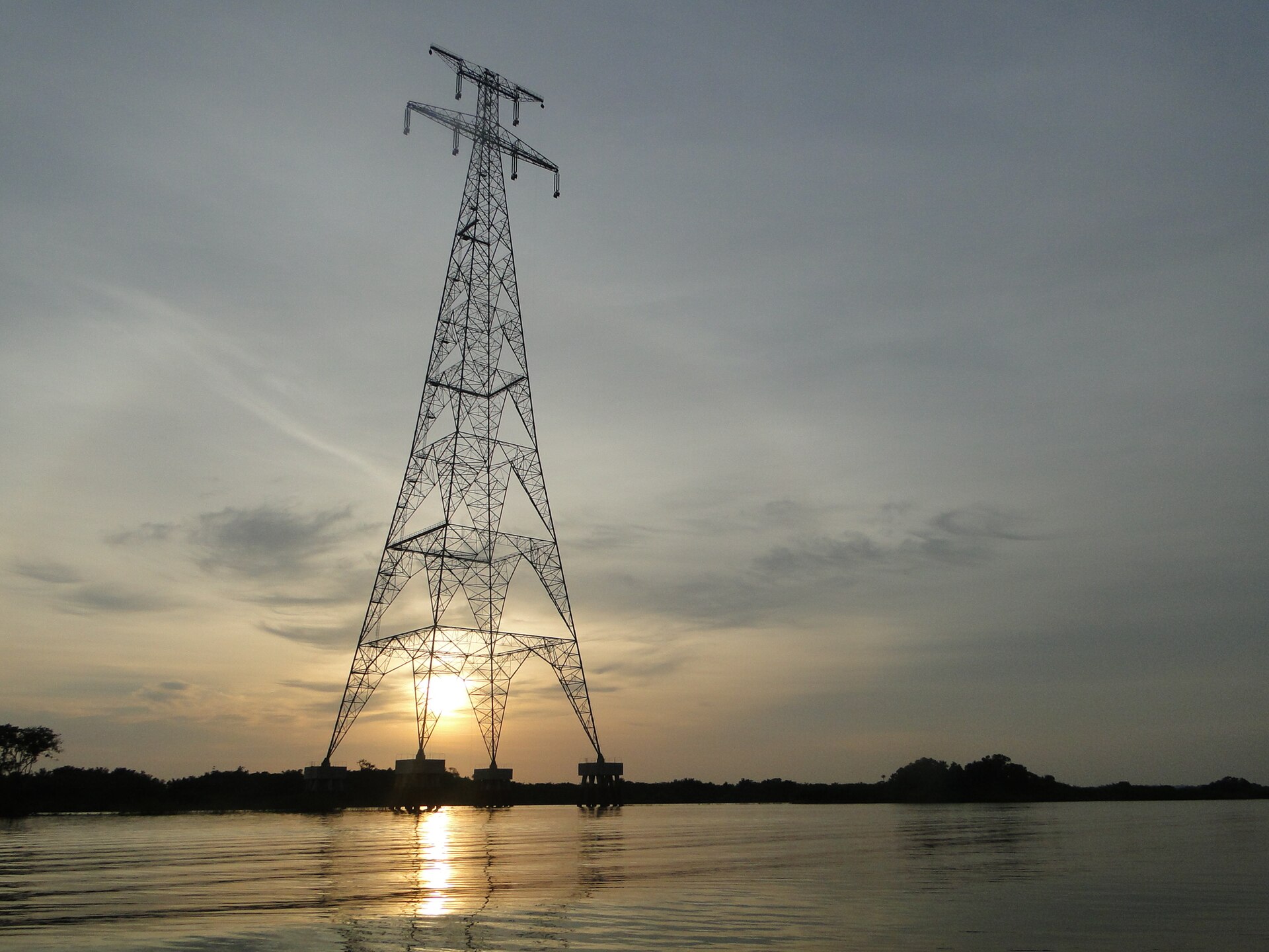 Torre de linha de transmissão de energia de alta tensão sobre rio na Amazônia, ao pôr do sol